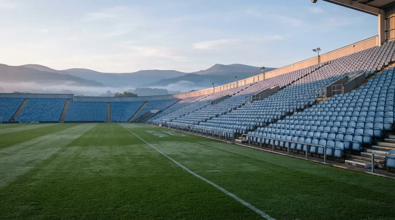 Ein leeres Stadion im Morgenlicht mit Blick auf die Sitzreihen, im Hintergrund Hügel und aufsteigender Nebel.