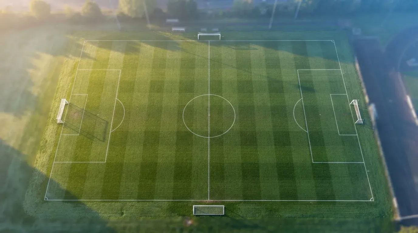 Ein Fussballplatz von oben gesehen, die Linien bilden ein helles Muster auf dem Rasen, Drohnenperspektive in der Morgendämmerung.