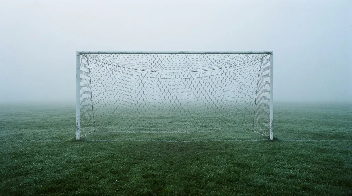 Eine Torlinie mit Netz steht am frühen Morgen im dichten Nebel auf einem Rasenplatz, die Umrisse der Pfosten verschwimmen.