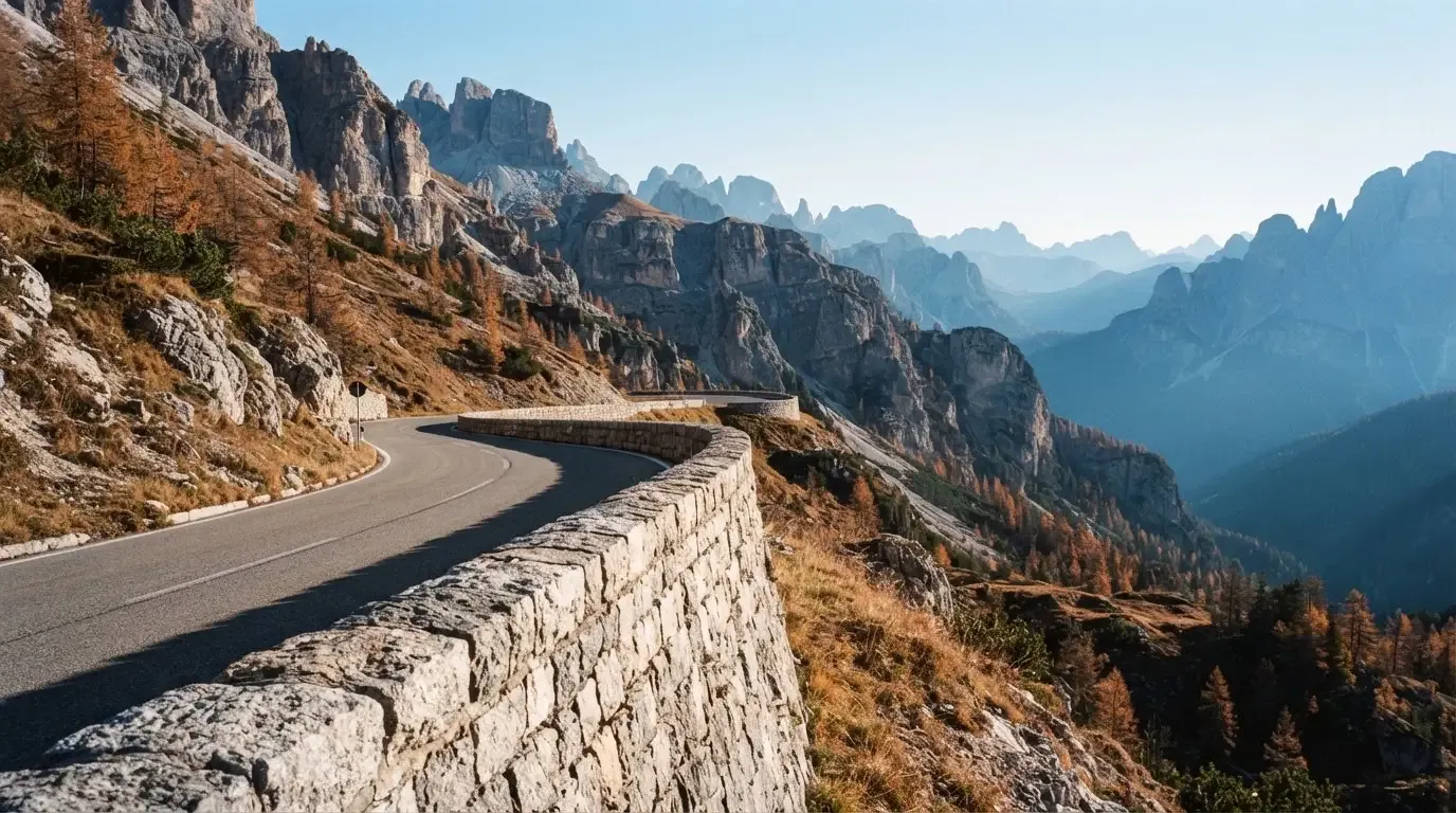 Eine Passstrasse im Hochgebirge säumt eine niedrige Steinmauer, dahinter ragen Felswände auf und der Herbsthimmel ist klar.