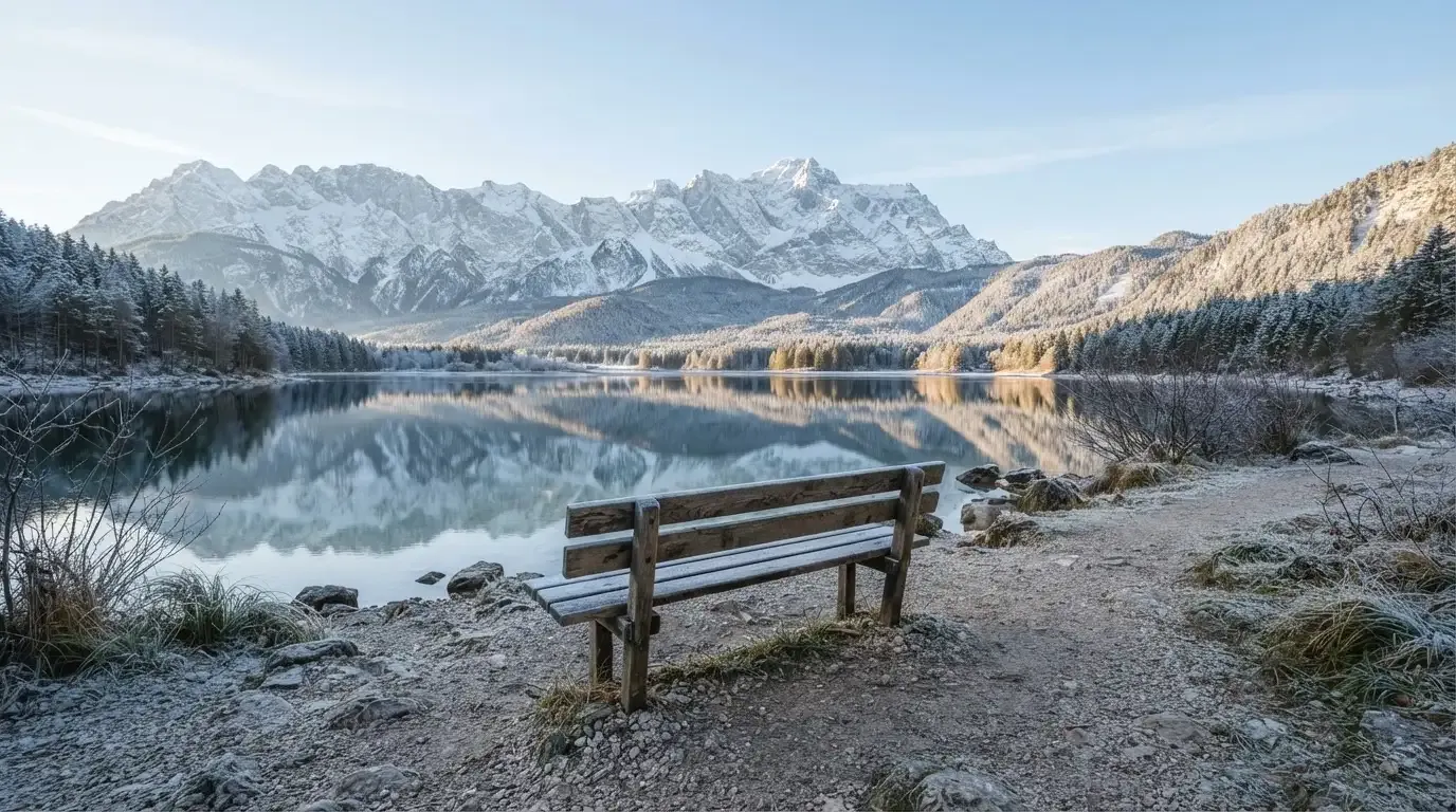 Eine Bank an einem Bergsee, dahinter schneebedeckte Gipfel im klaren Licht eines Wintermorgens.