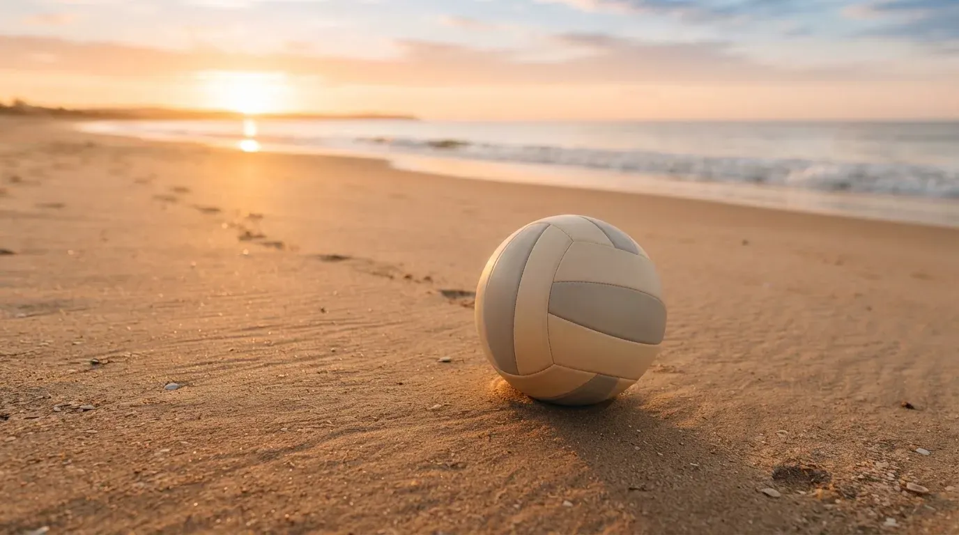 Ein Volleyball liegt auf feinem Sand an einem leeren Strand bei Sonnenaufgang.