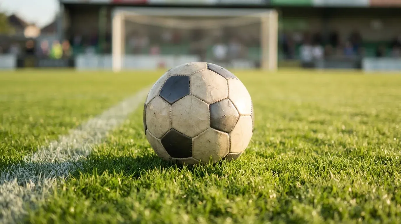 Ein Fussball auf dem Rasen aus niedriger Perspektive aufgenommen, die Torpfosten verschwimmen im Hintergrund.