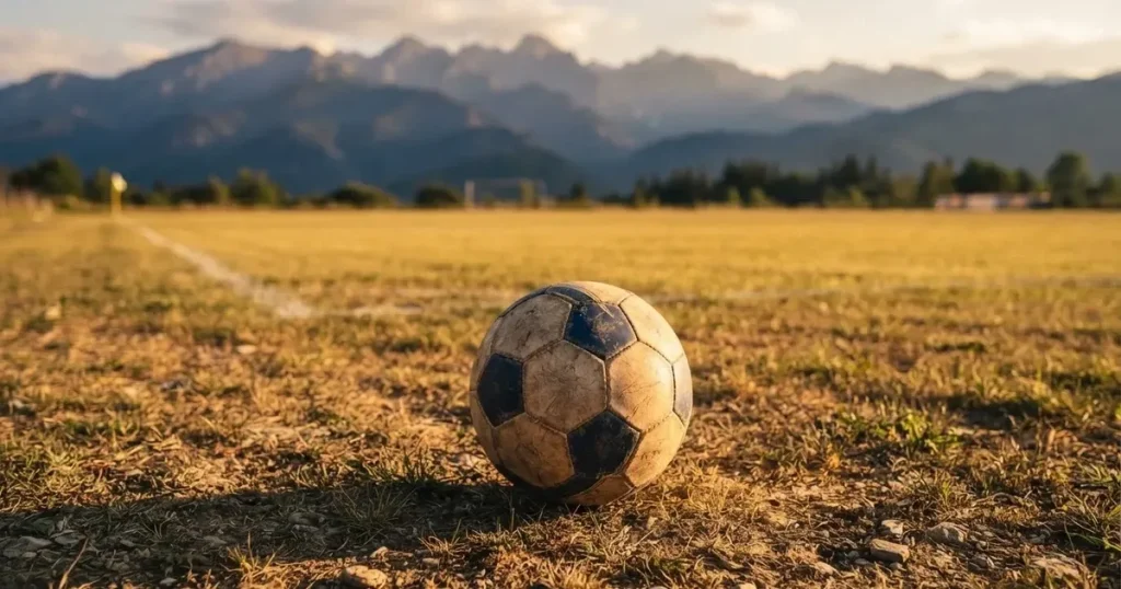 Ein Fussball auf einem staubigen Rasenstück in der Abendsonne, im Hintergrund eine hohe Bergkette