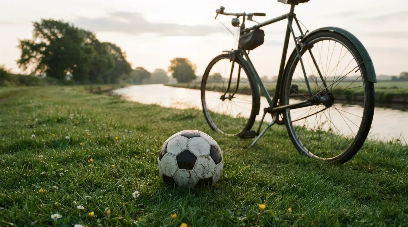 Ein Fussball liegt auf einer Wiese neben einem Fahrrad, im Hintergrund ein Kanal im Morgenlicht