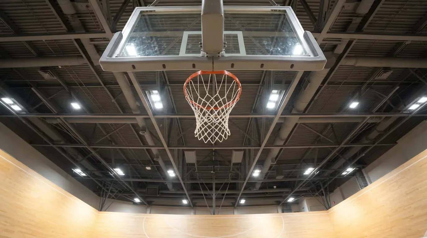 Ein Basketballkorb von unten gesehen, darüber eine Hallendecke mit Scheinwerfern und Stahlträgern.