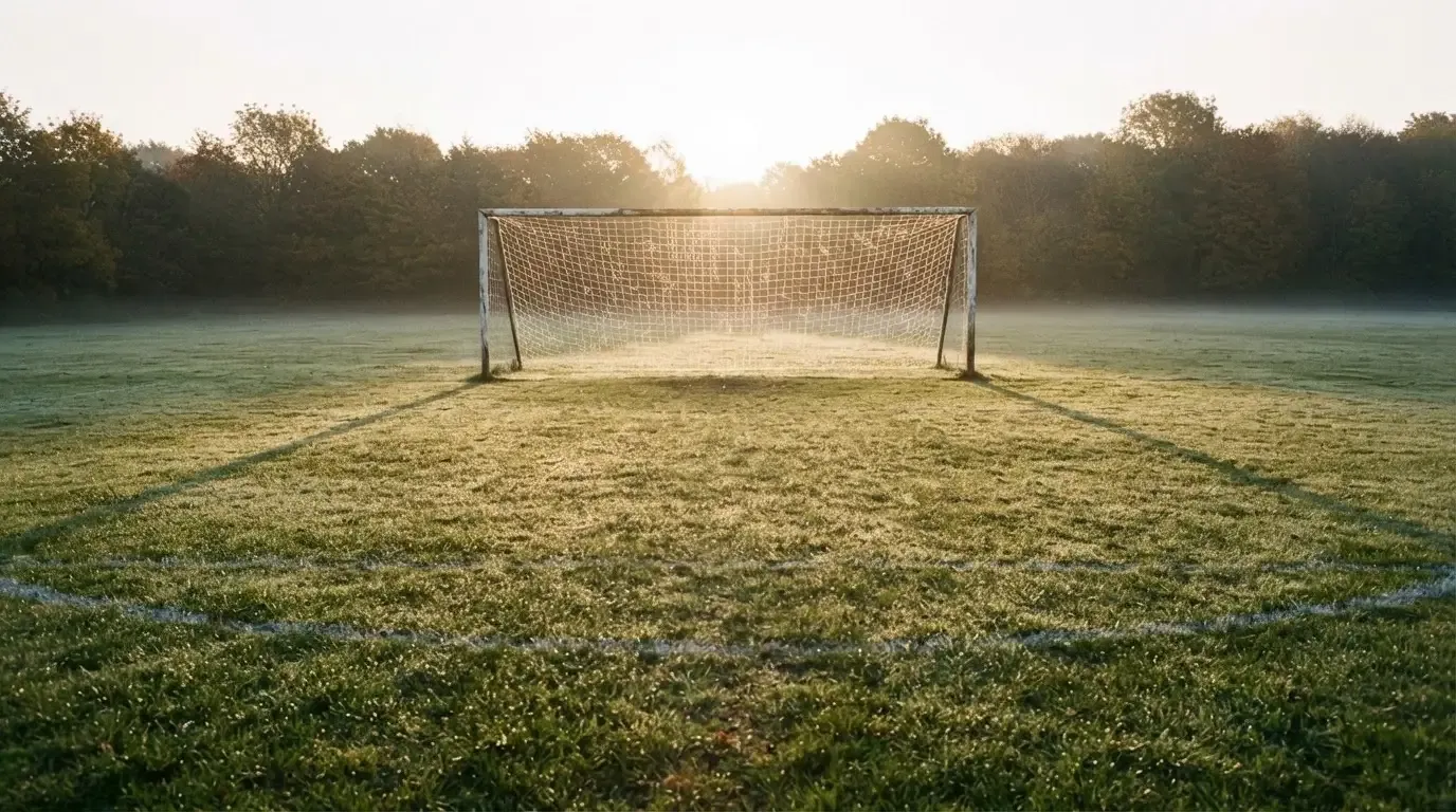 Ein Fussballtor mit Netz in der Totalen auf einem leeren Platz, Tau glänzt im Gras und die Morgensonne steht tief.