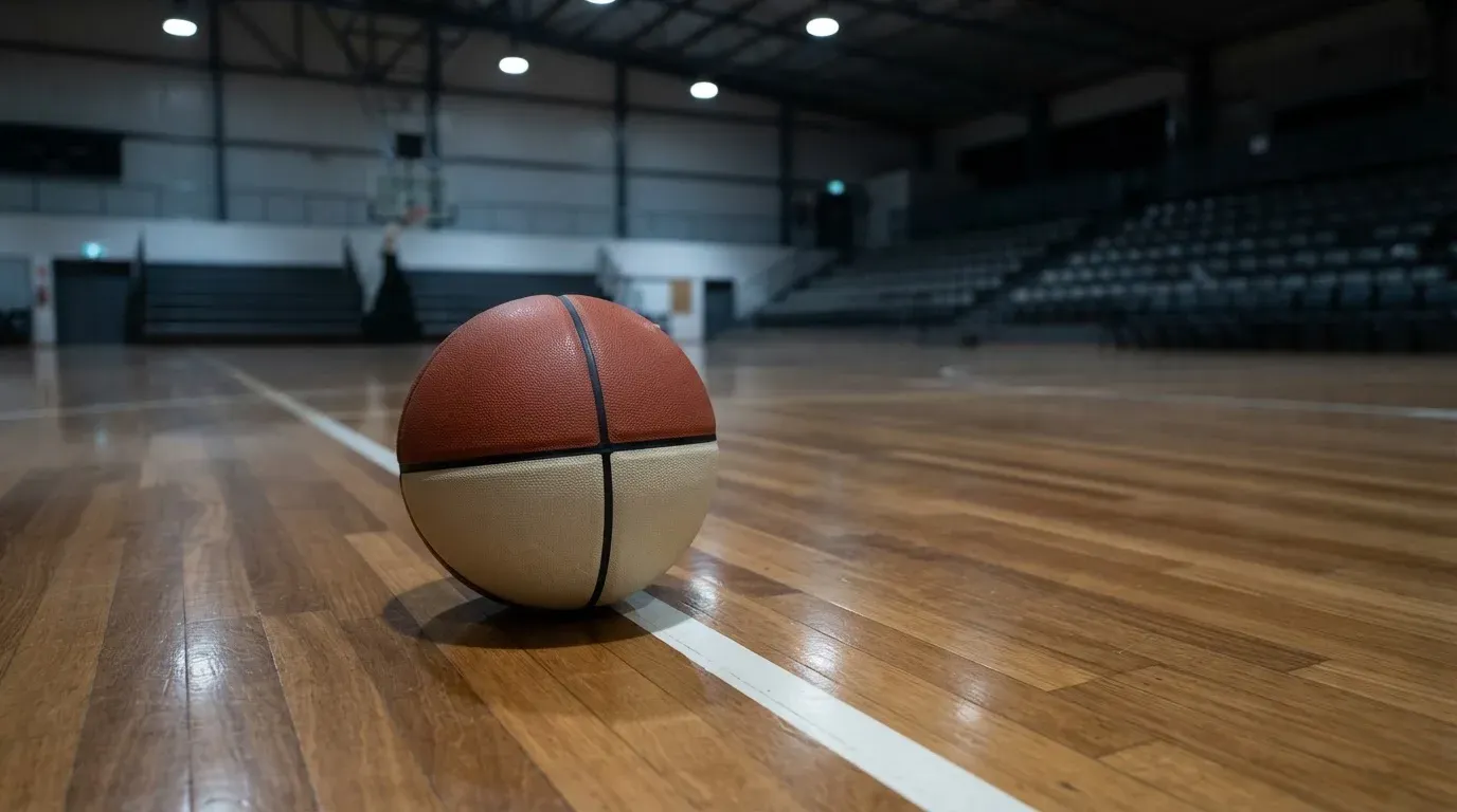 Ein Basketball liegt auf dem Parkett einer leeren Sporthalle im Licht der Deckenlampen.