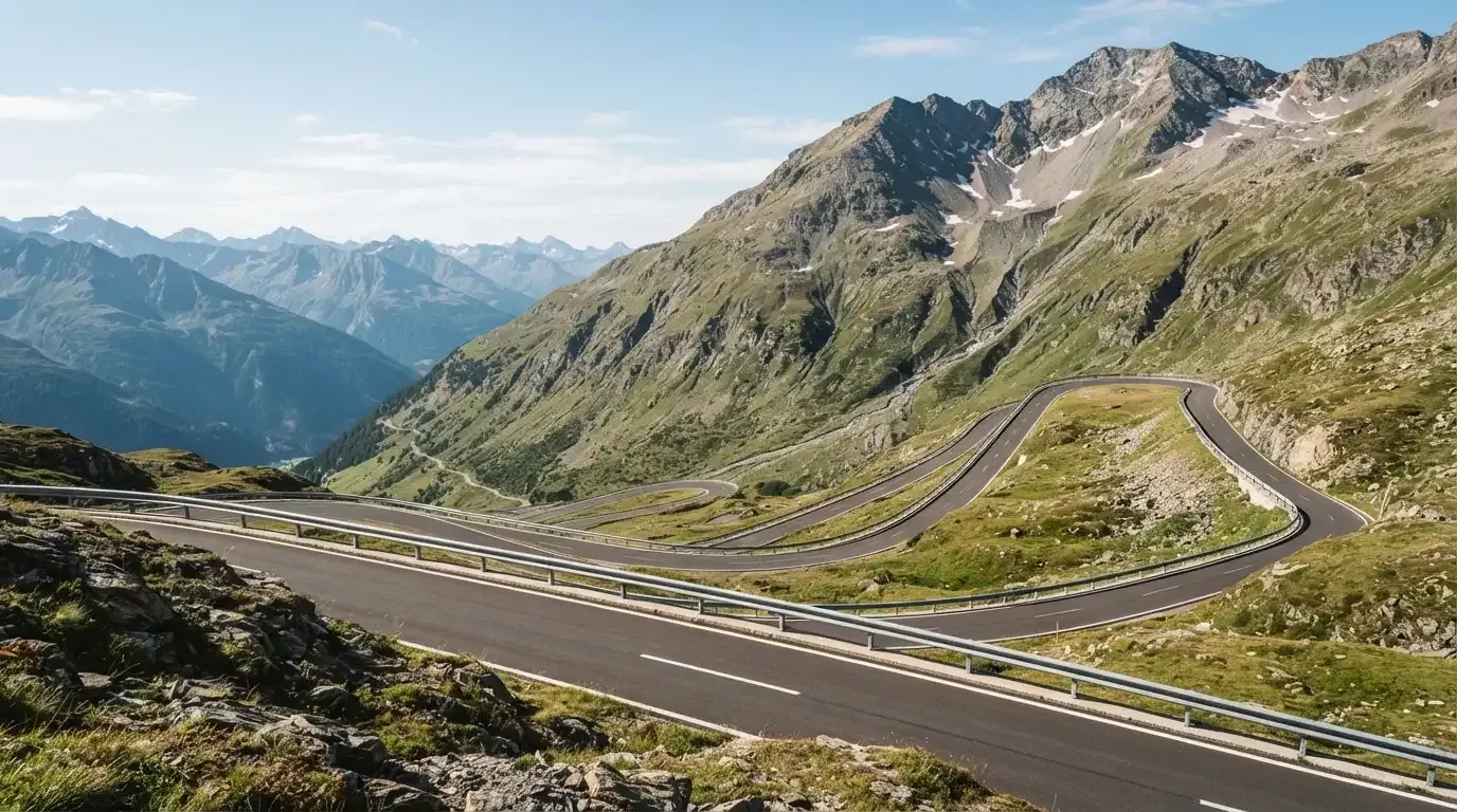 Eine Passstrasse mit Leitplanke windet sich an einem klaren Tag durch eine Berglandschaft.