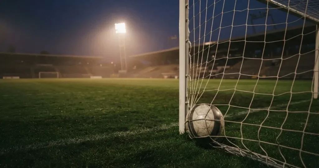 Ein Fussball liegt im Netz eines Tores, Flutlicht und kalte Abendluft liegen über dem leeren Platz