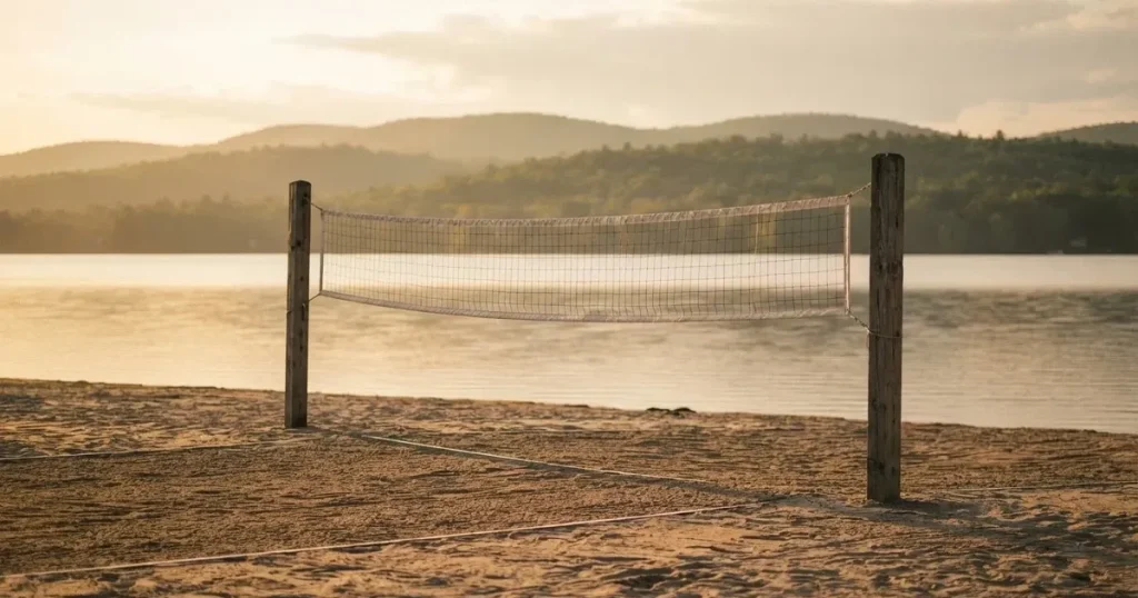 Ein Volleyballnetz am Sandstrand eines Sees, späte Nachmittagssonne, das Wasser liegt glatt im Hintergrund