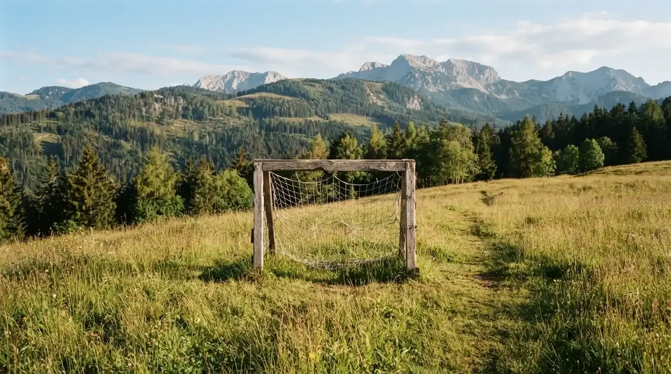 Eine Almwiese mit einem kleinen Holztor für Kinderfussball, dahinter erheben sich bewaldete Hänge im Nachmittagslicht.