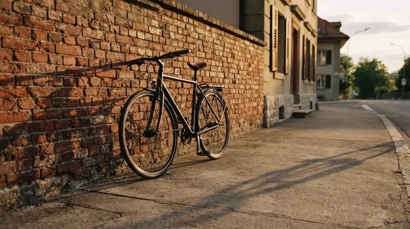 Ein Fahrrad lehnt an einer Backsteinmauer, auf dem Gehweg davor fallen lange Schatten.